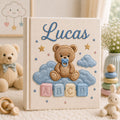 Personalized hand embroidered photo album featuring a teddy bear with a pacifier sitting on clouds above colorful ABC blocks on a linen cover