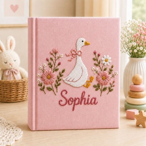 Personalized hand embroidered photo album featuring a white goose with pink bow surrounded by delicate pink flowers and custom name embroidery on linen cover