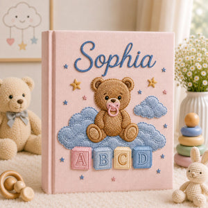 Personalized hand embroidered photo album featuring a teddy bear with a pacifier sitting on clouds above colorful ABC blocks on a linen cover