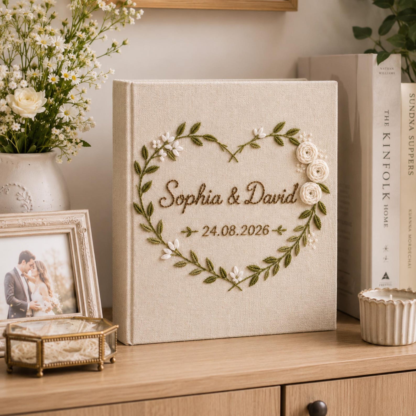 Personalized embroidered wedding photo album with heart-shaped floral wreath, white rose embroidery, botanical greenery, custom couple names, wedding date, and elegant linen hardcover design