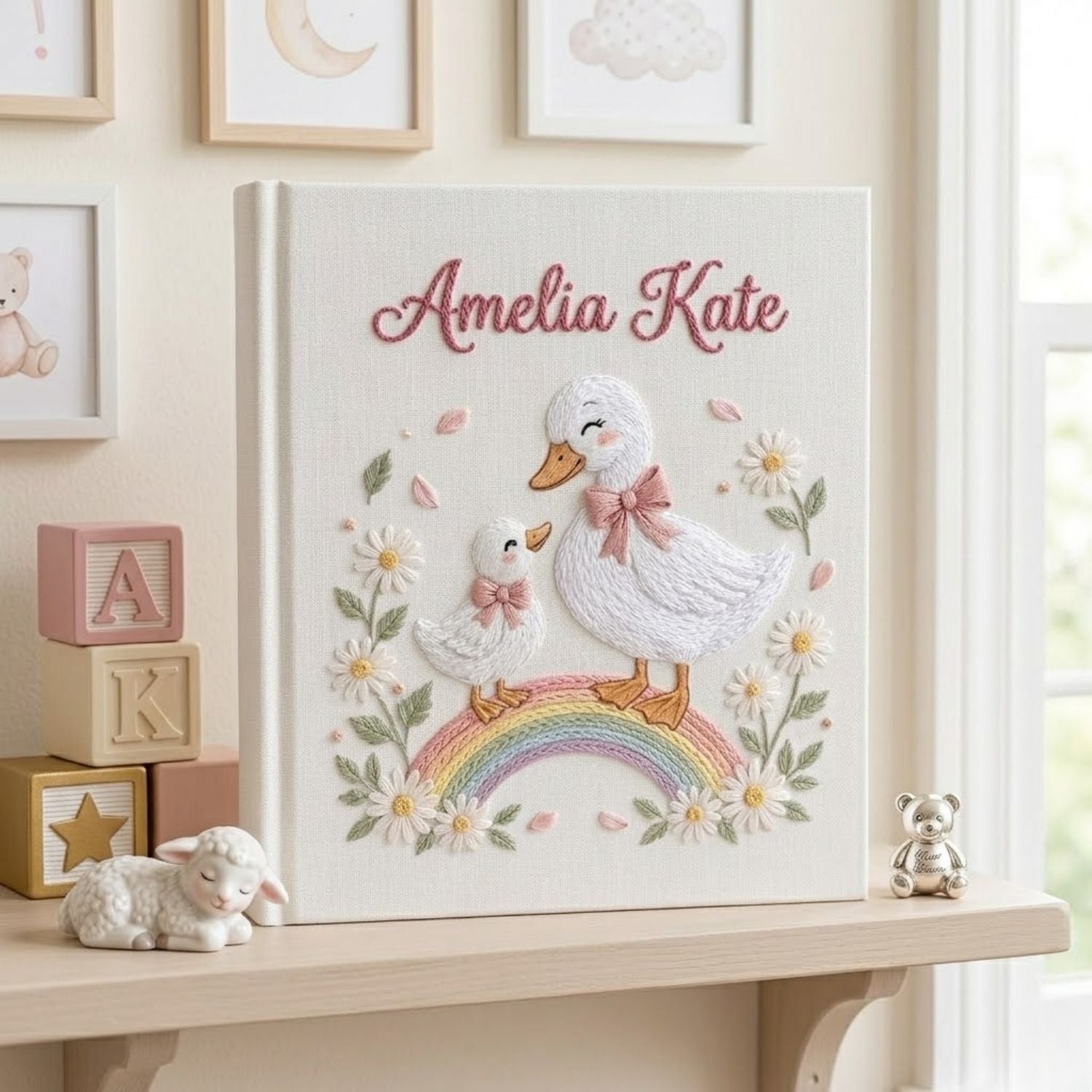 Personalized hand embroidered photo album featuring a swan mother and baby standing on a pastel rainbow surrounded by daisies and floral details