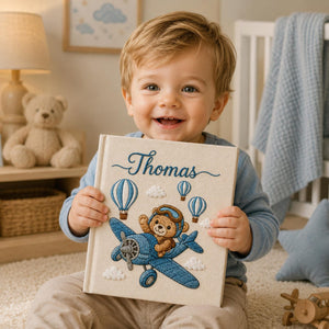 Personalized embroidered baby photo album featuring teddy bear pilot flying a vintage blue airplane with hot air balloons and clouds