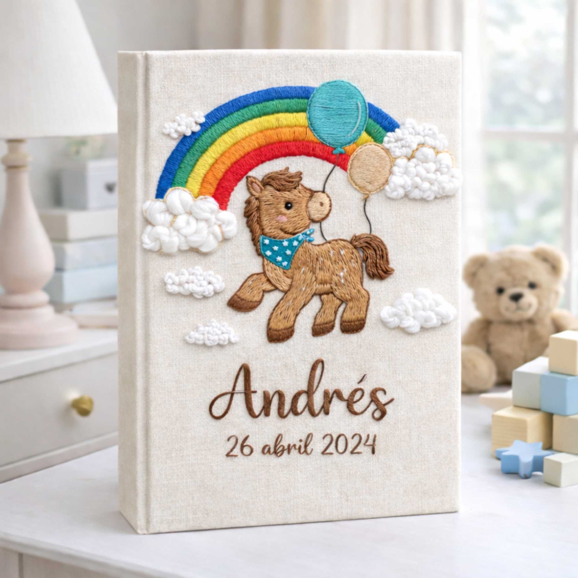 Personalized hand embroidered photo album featuring an adorable pony with balloons, colorful rainbow, fluffy clouds, and custom name embroidery on linen cover