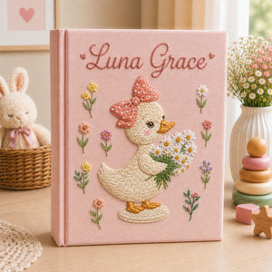 Personalized hand embroidered photo album featuring a cute duckling with a polka dot bow holding a daisy bouquet surrounded by pastel flowers and custom name embroidery