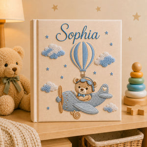 Personalized hand embroidered photo album featuring a teddy bear pilot flying a vintage airplane with hot air balloons, clouds and stars