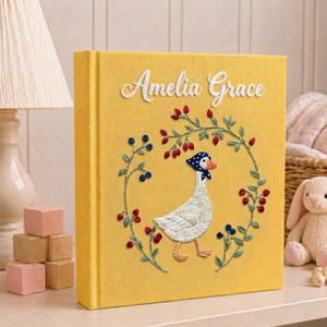Personalized hand embroidered photo album featuring an elegant goose surrounded by a floral berry wreath on a golden linen cover