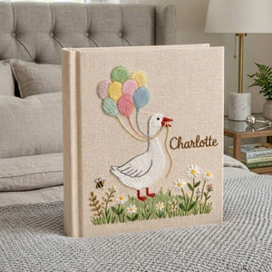 Personalized goose hand embroidered baby photo album with pastel balloons and floral meadow design on linen cover