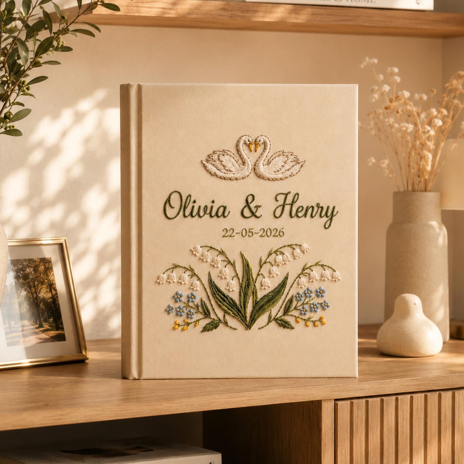 Personalized embroidered wedding photo album with swan embroidery, lily of the valley flowers, botanical details, custom couple names, wedding date, and elegant linen hardcover design