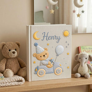 Personalized hand embroidered baby photo album featuring teddy bear driving a pastel blue vintage car with balloon, moon, stars, and sunshine accents