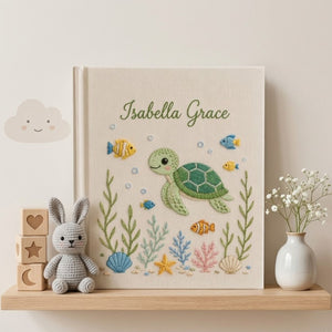 Personalized hand embroidered photo album featuring a cute sea turtle swimming with tropical fish, coral, seashells, and ocean plants on a premium linen cover customized with a baby name