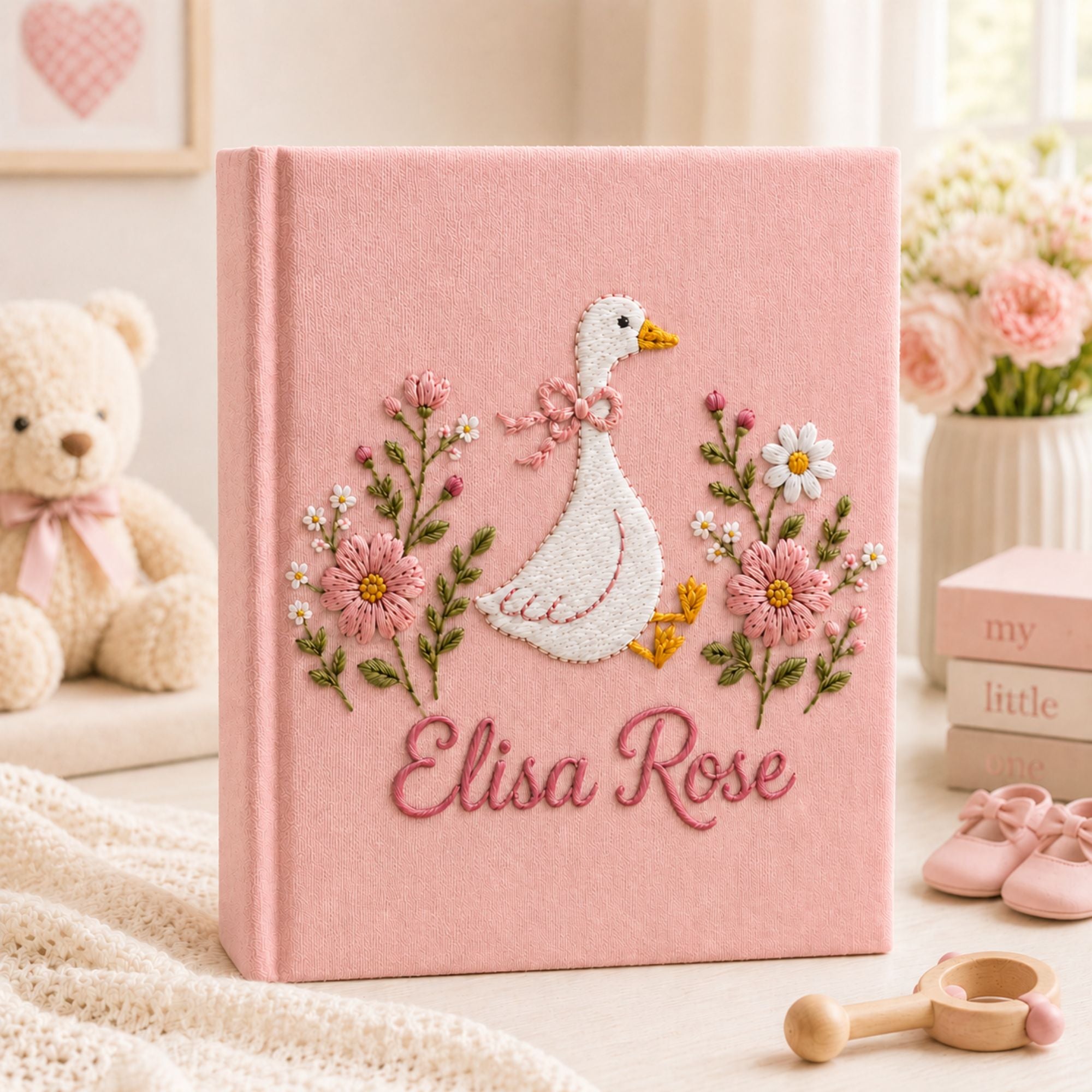 Personalized hand embroidered photo album featuring a white goose with pink bow surrounded by delicate pink flowers and custom name embroidery on linen cover