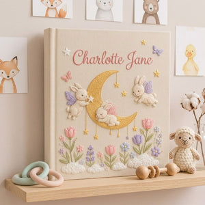 Personalized hand embroidered photo album featuring fairy bunnies around a golden crescent moon with stars, flowers, butterflies, and clouds on a premium linen cover customized with a baby name