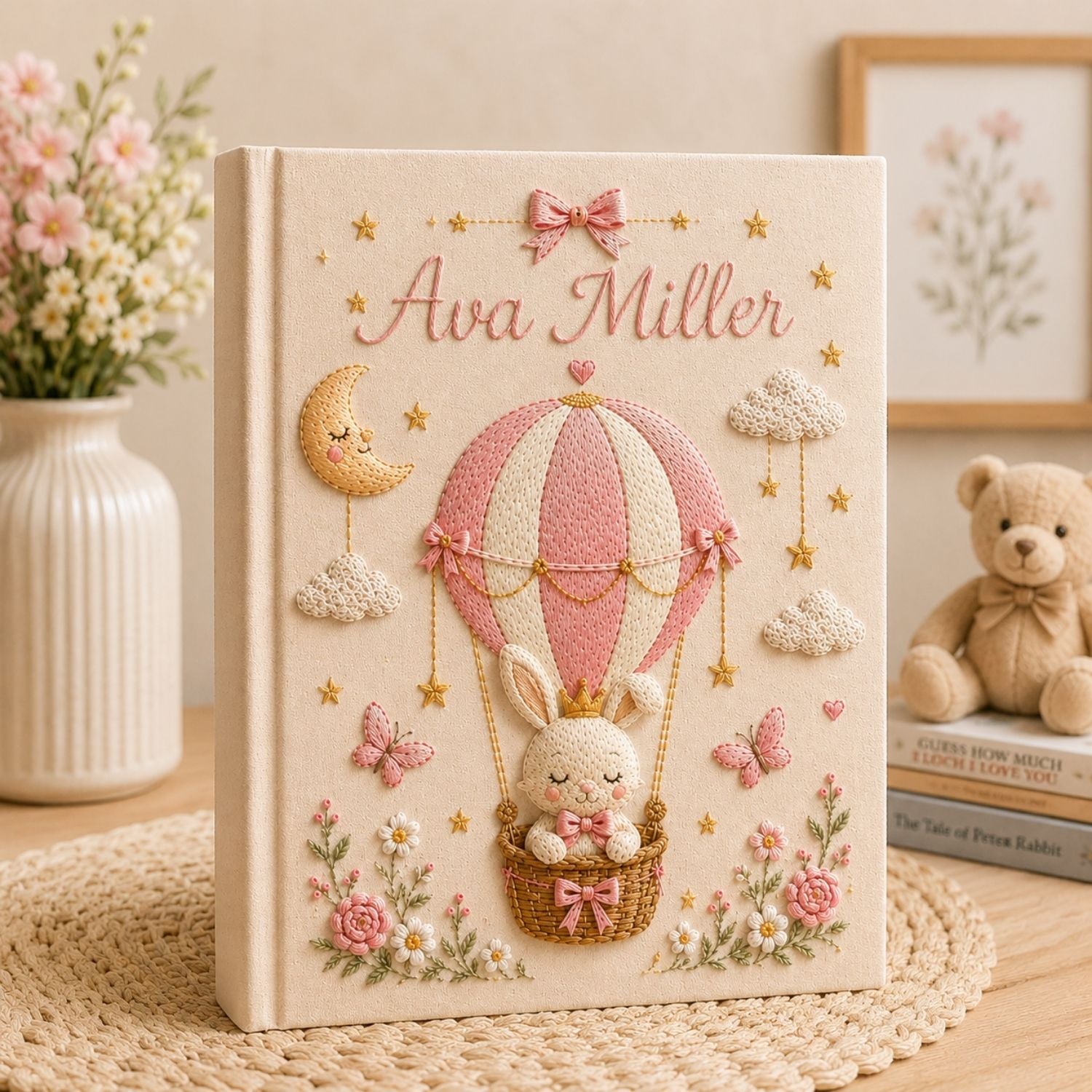 Personalized hand embroidered photo album featuring a crowned bunny in an elegant balloon basket beneath a sleepy crescent moon with hanging stars, butterflies, clouds, flowers, and custom name embroidery on a premium linen cover