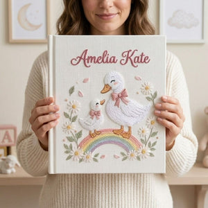 Personalized hand embroidered photo album featuring a swan mother and baby standing on a pastel rainbow surrounded by daisies and floral details