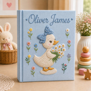Personalized hand embroidered photo album featuring a cute duckling with a polka dot bow holding a daisy bouquet surrounded by pastel flowers and custom name embroidery