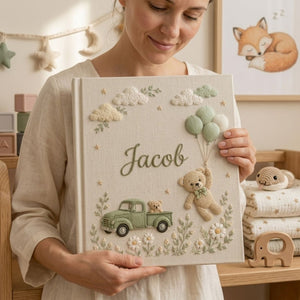 Personalized hand embroidered photo album featuring a vintage sage green pickup truck, floating teddy bear with balloons, clouds, and wildflowers on a premium linen cover customized with a baby name