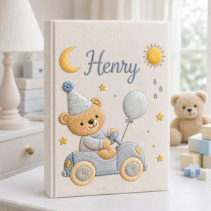Personalized hand embroidered baby photo album featuring teddy bear driving a pastel blue vintage car with balloon, moon, stars, and sunshine accents