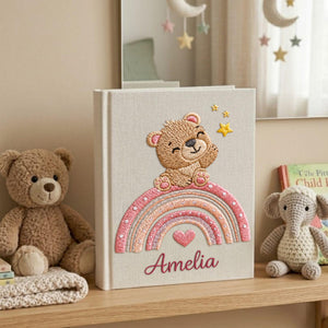 Personalized hand embroidered baby photo album featuring teddy bear sitting on pastel rainbow with stars and heart accents